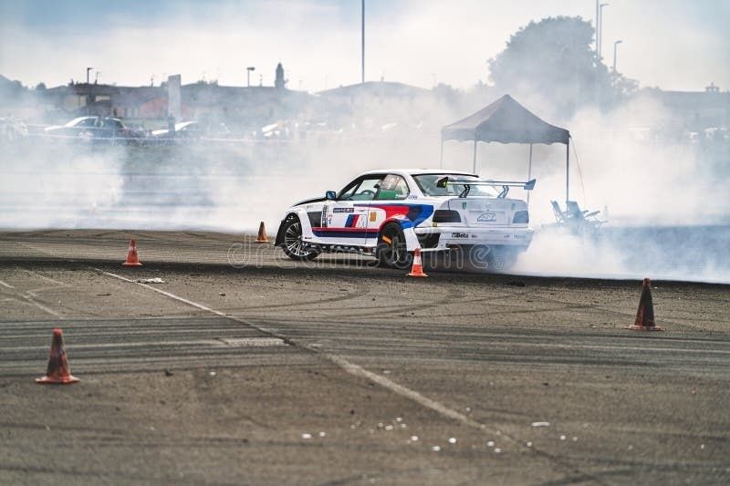 White race car drifting between cones, surrounded by tire smoke