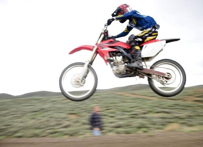 Rider launches a red off-road motorcycle over a grassy dirt section